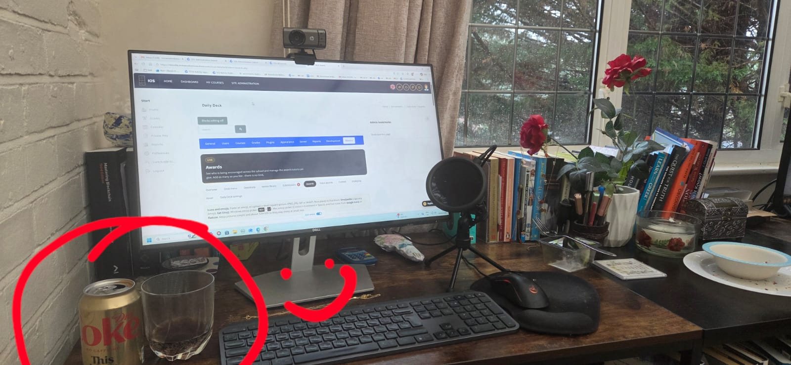 A desk by a window with books, a microphone and a monitor.