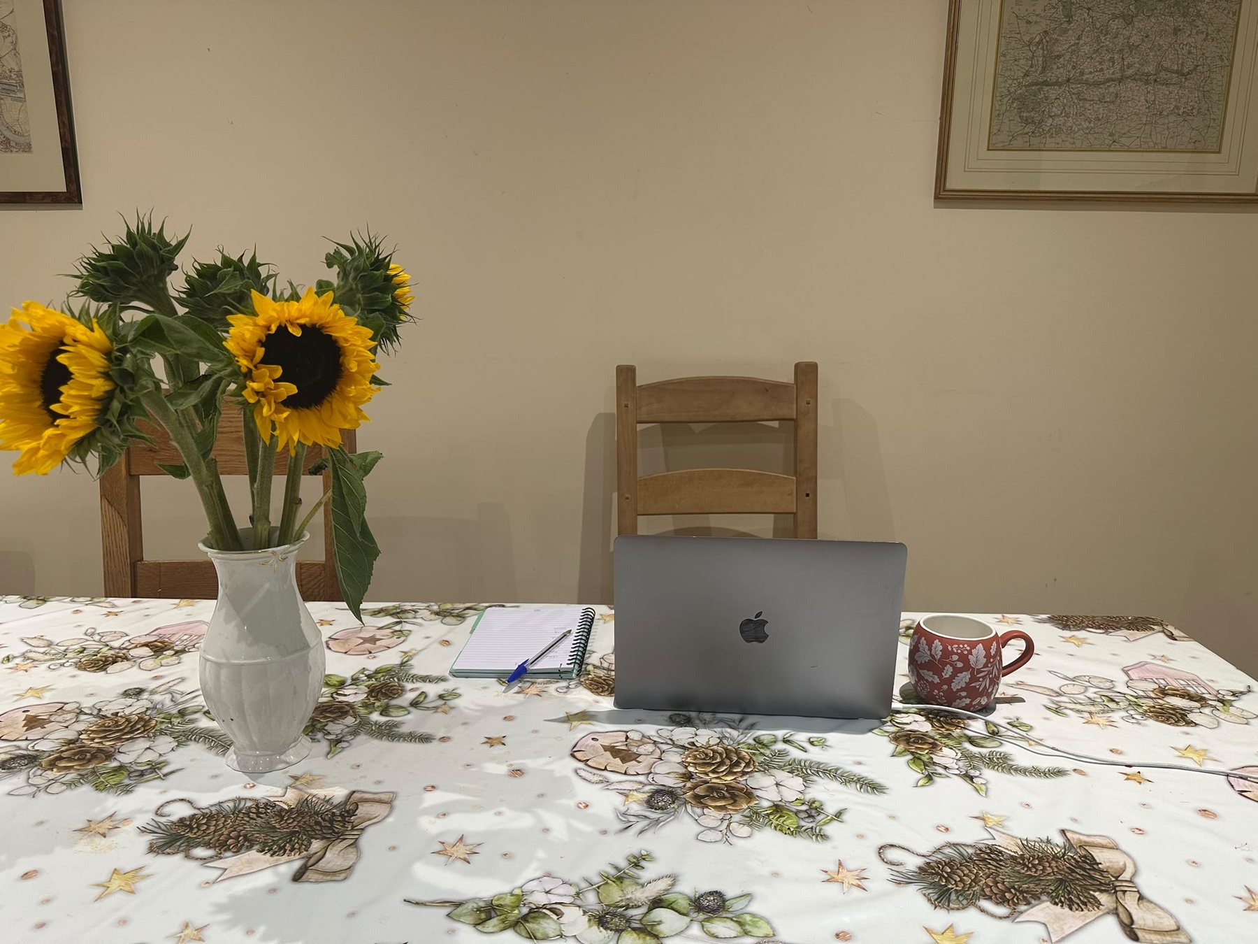 A kitchen table with sunflowers, a laptop, a notebook and a pen.