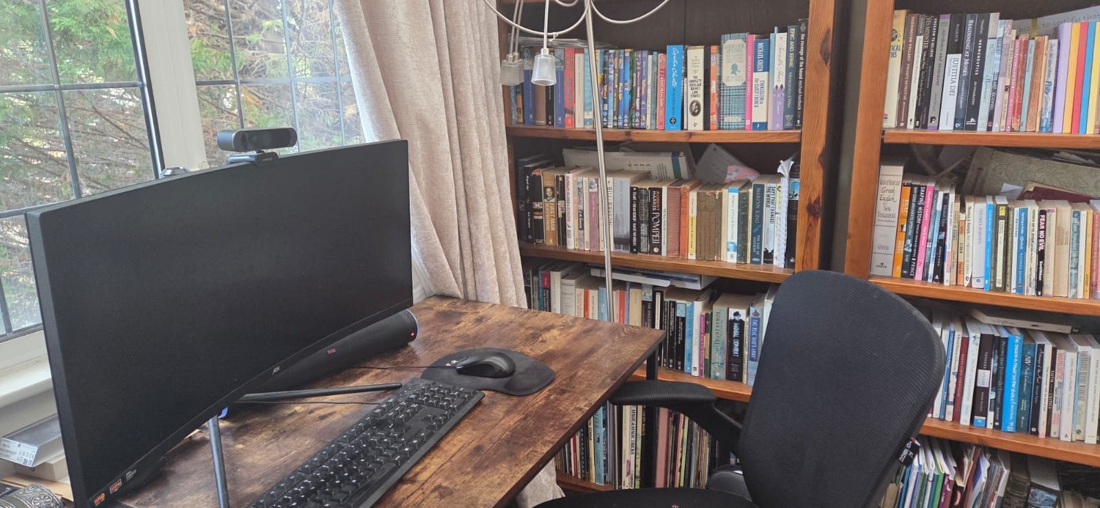 A desk by a window, with bookshelves filling the wall.