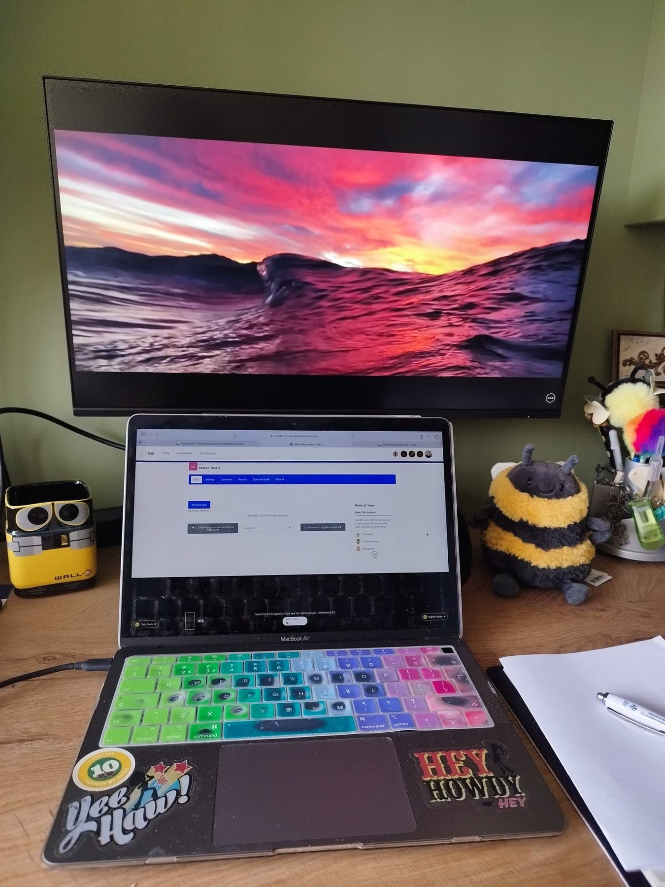 A laptop on a wooden desk, paper and a pen to the side.